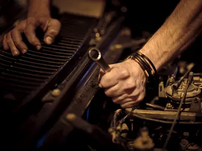 A mechanic’s hands using a wrench on a car engine under warm shop lighting