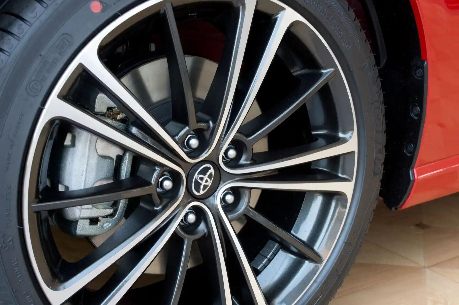 A front disc brake and caliper behind the spokes of an alloy wheel, the parts Floorjack Auto Repair inspects on a Phoenix brake job