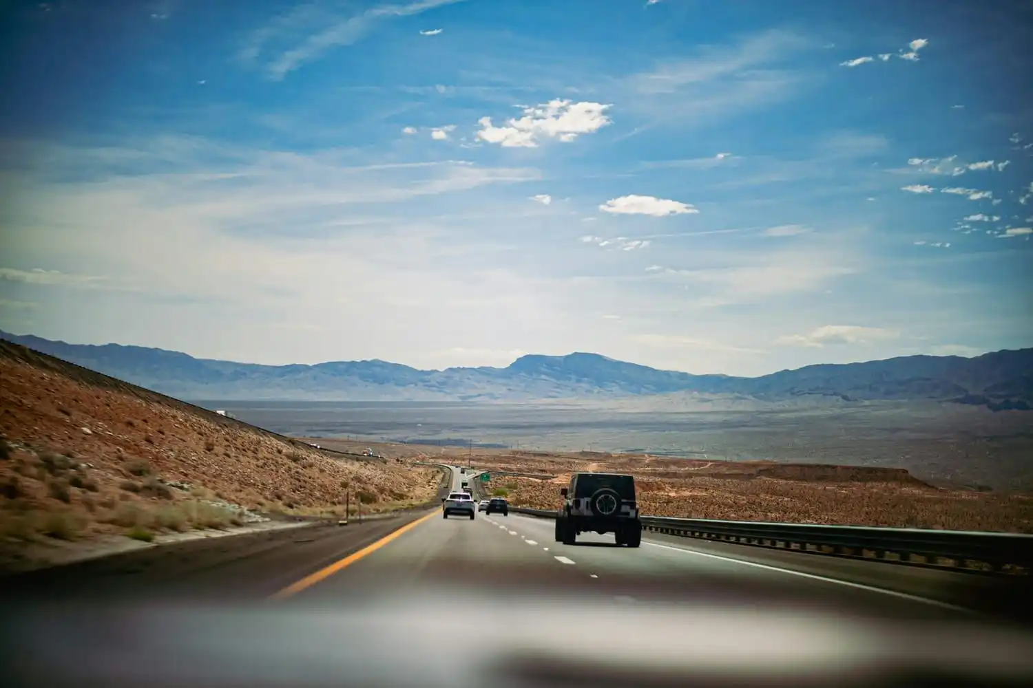 A driver’s view through the windshield of vehicles on a desert freeway heading toward distant mountains