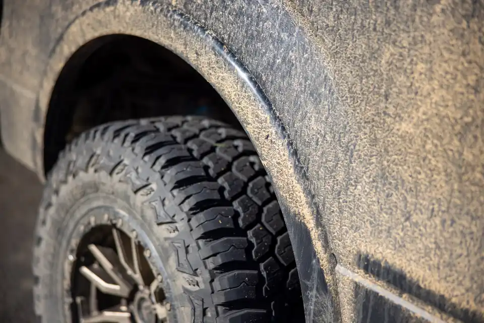 Close-up of a work truck's dust-caked front fender and mud-terrain tire, the kind of diesel Floorjack Auto Repair services in Deer Valley