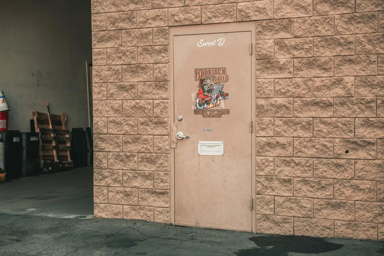 The back of the Floorjack Auto Repair building in Phoenix, with the service door marked Sweet D set into the block wall beside an open bay