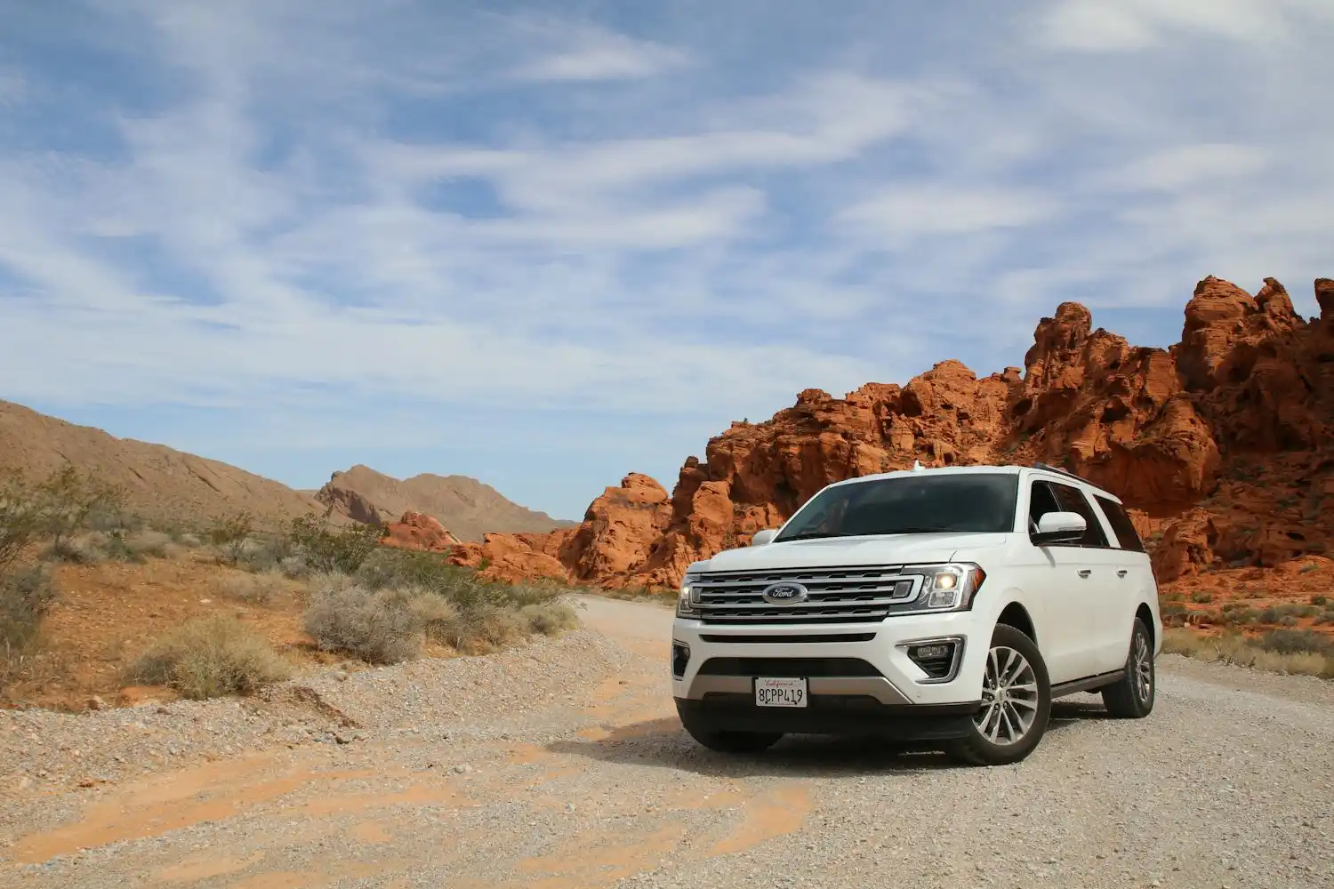 A white Ford SUV parked on a desert road below red rock cliffs under a clear Arizona sky