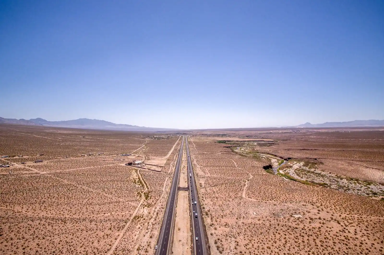 A divided highway running straight through open Arizona desert toward a distant mountain range, seen from the air