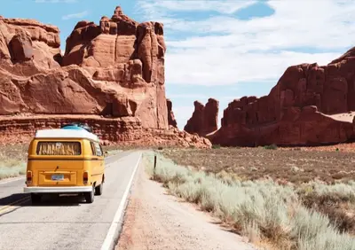 A vehicle on an open desert highway winding past red rock formations in Arizona