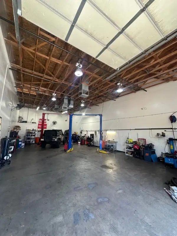 Inside the Floorjack Auto Repair service bay in Phoenix — a Jeep Wrangler on the two-post lift beneath an open-truss ceiling, with tool benches and equipment along the walls